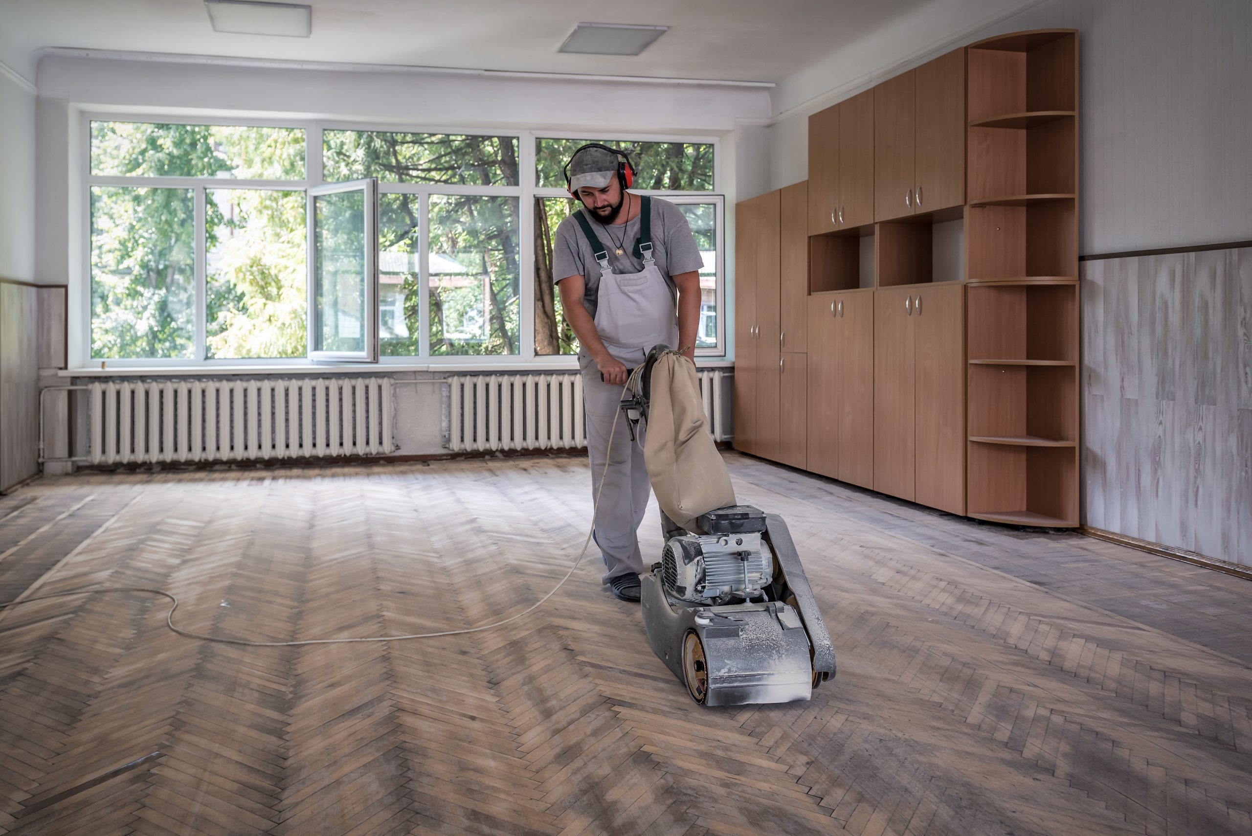 Technician using a professional sanding machine with built-in extraction to perform Dust-Free Floor Sanding on an oak block parquet floor in a Stanmore property.