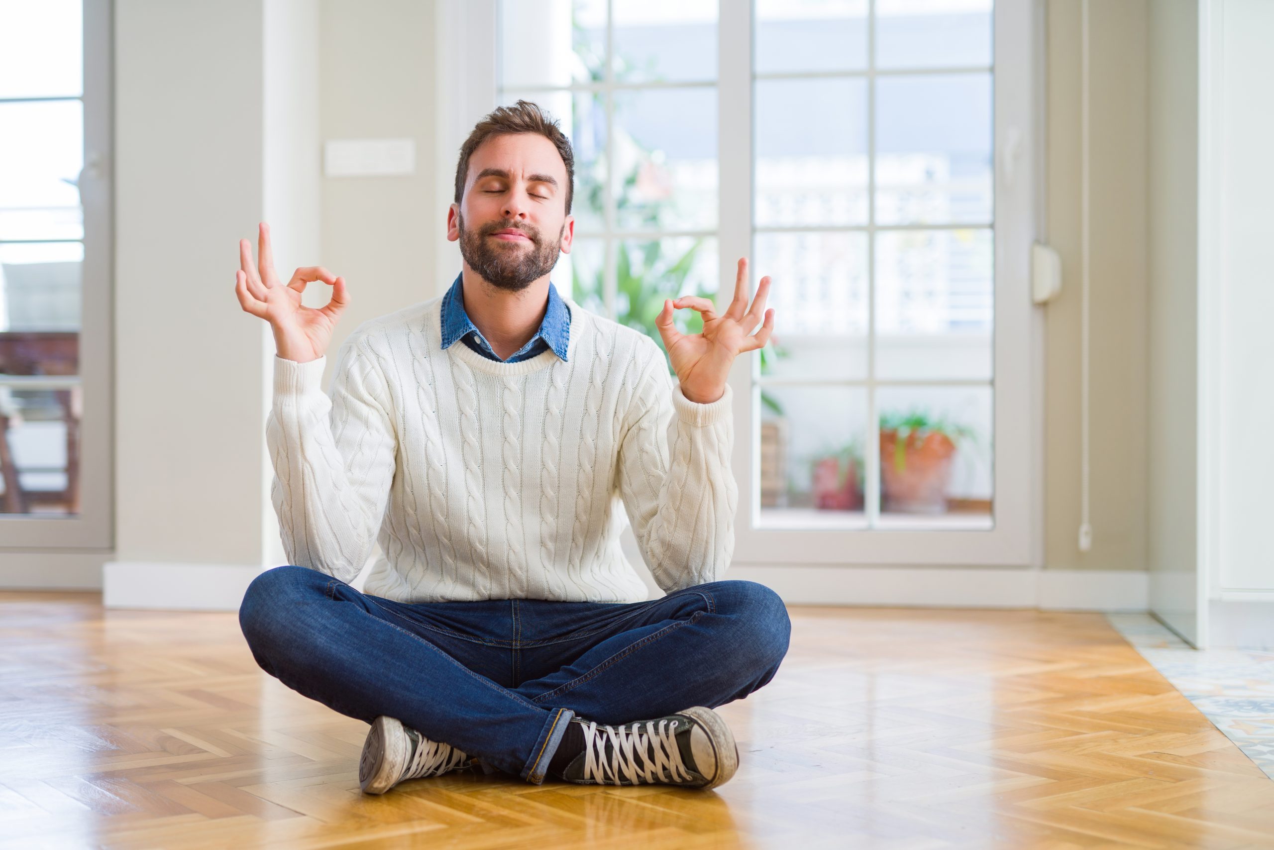Man sitting cross-legged in a relaxed meditation pose on a freshly refinished oak herringbone parquet floor in a Stanmore home, demonstrating the calm and cleanliness achieved through Dust-Free Floor Sanding.
