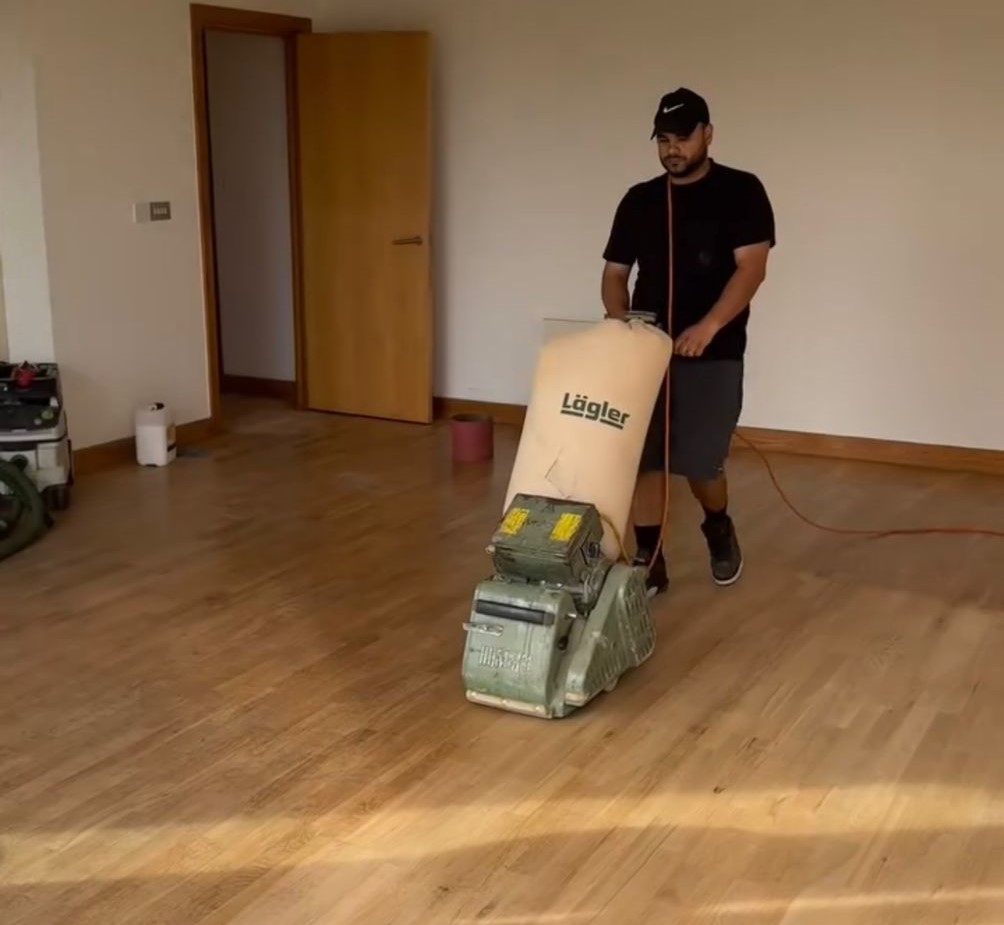 Wood Floor Sanding in Stanmore – technician sanding a light oak plank hardwood floor in an empty living room.