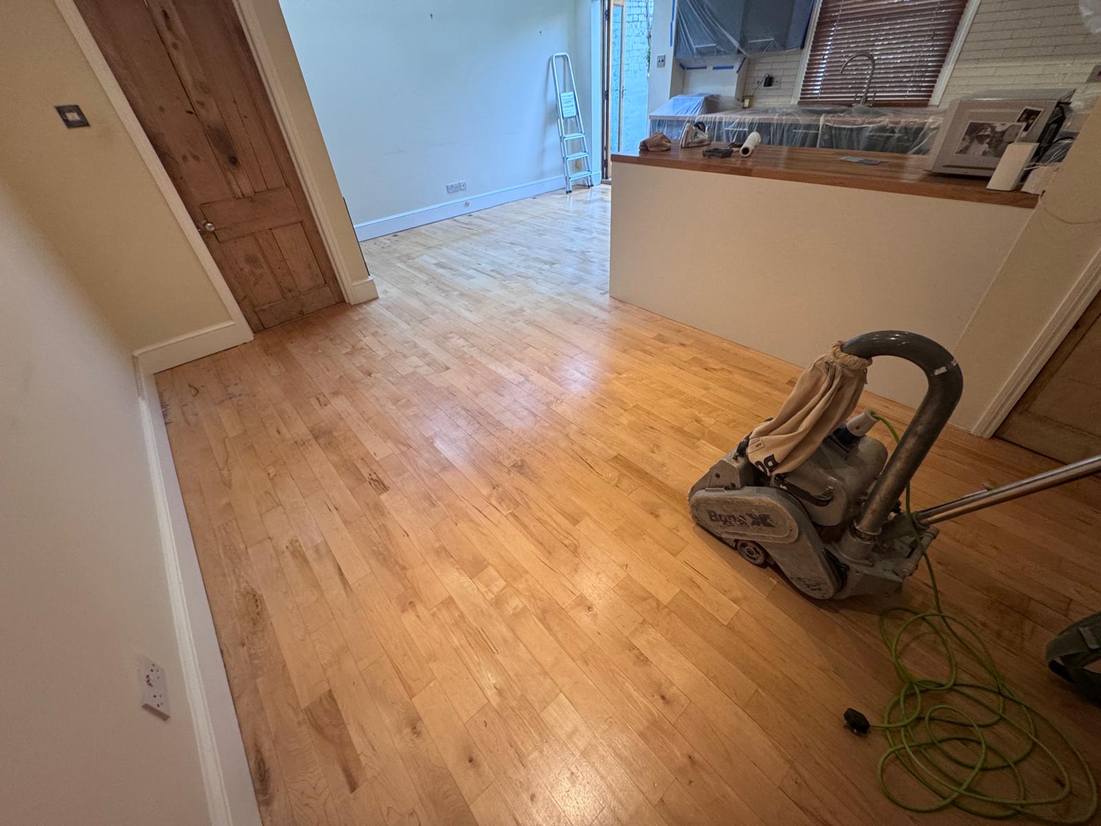 Wood Floor Sanding in Stanmore – light oak strip hardwood floor being sanded in an open-plan living room and kitchen.