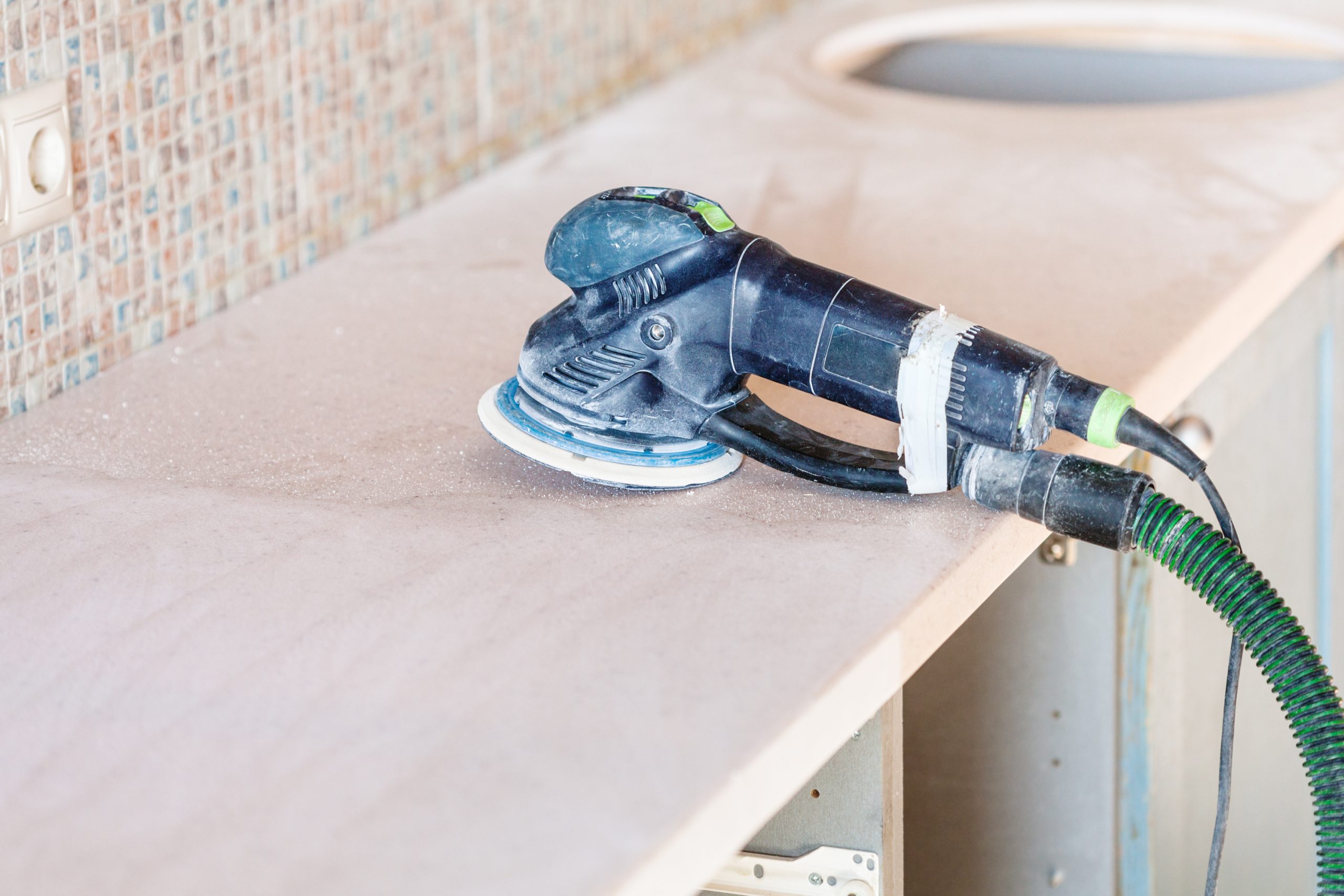 Dust-free sander on a beech butcher block hardwood kitchen worktop in Stanmore during professional Worktop Refinishing, with matching hardwood floor below.