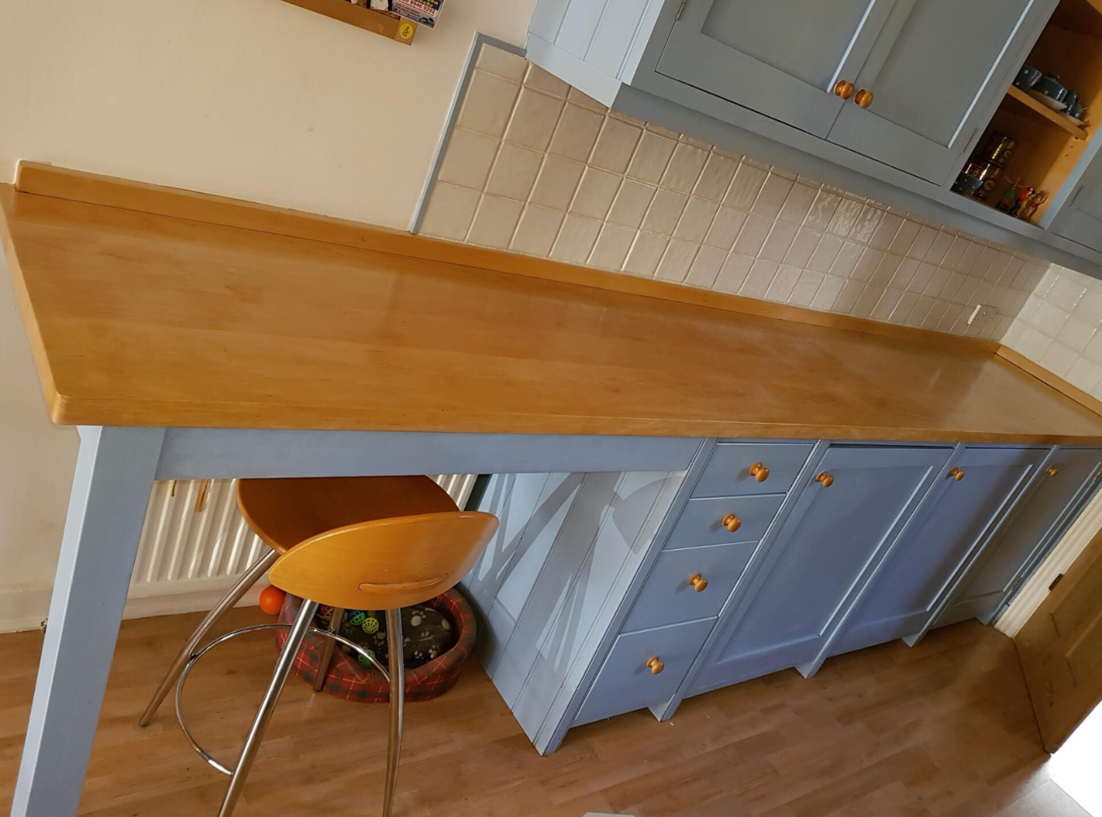Freshly restored solid wood kitchen worktop with blue cabinets and oak-effect laminate floor in a Stanmore home after expert Worktop Refinishing.
