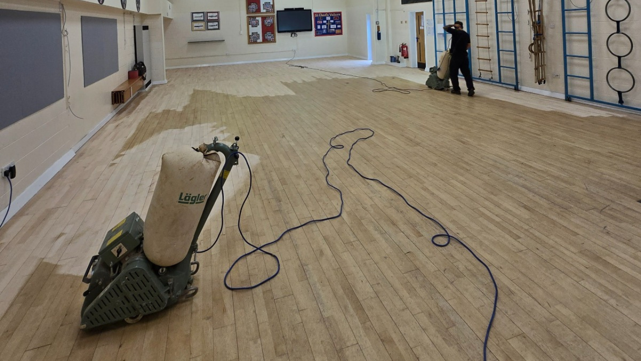 Wood Floor Sanding in Stanmore school hall, showing commercial sanding machines restoring large maple strip hardwood sports flooring.