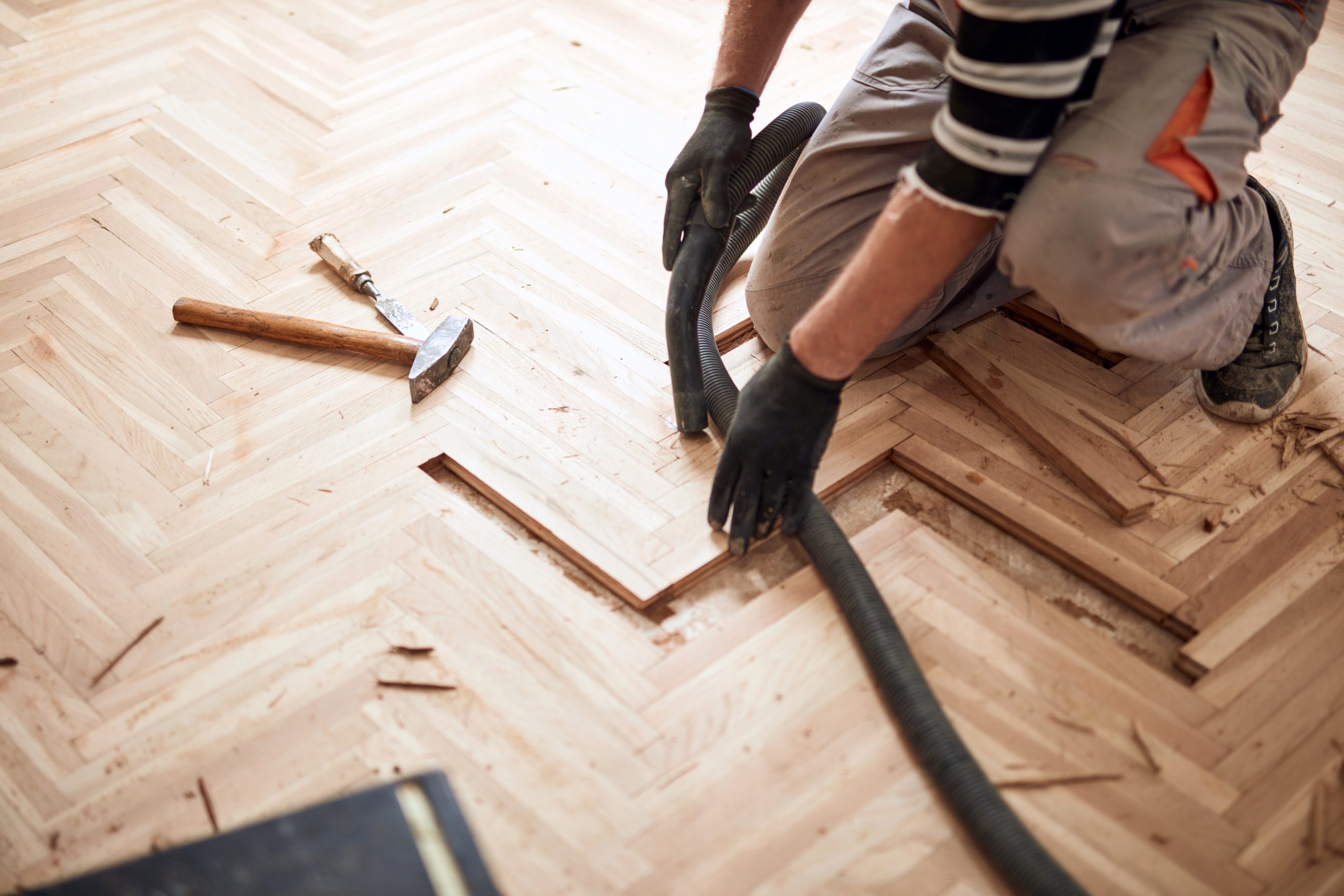 Wood Floor Sanding in Stanmore with parquet repair, showing a specialist replacing damaged light oak herringbone parquet blocks before sanding and refinishing.