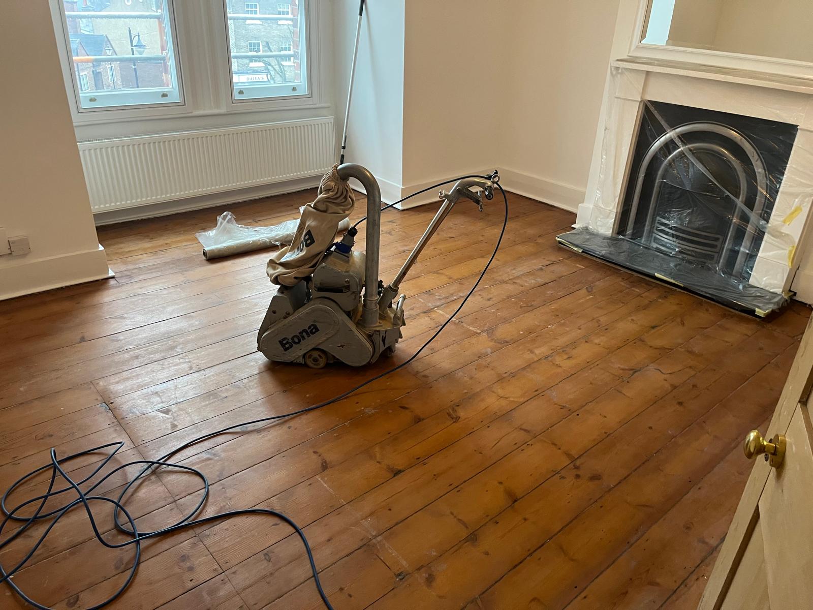 Wood Floor Sanding in Stanmore living room in progress, with professional sander preparing natural pine floorboards for refinishing.